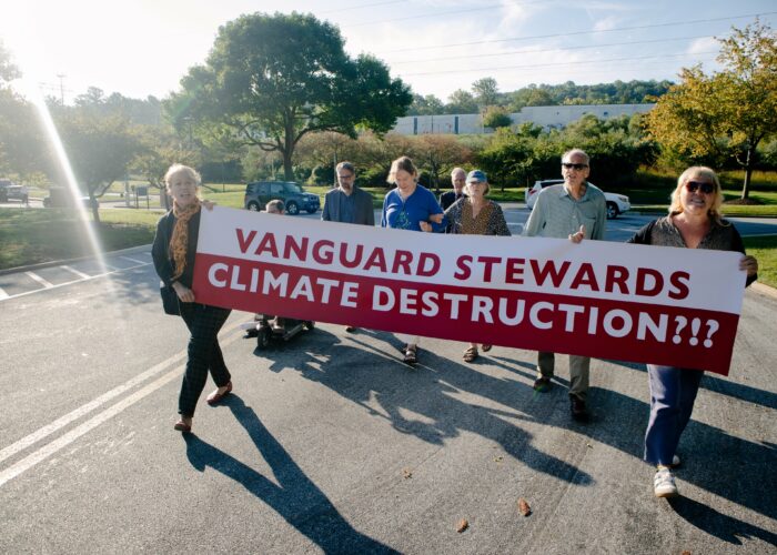 a group of people hold a large red and white banner that reads "Vanguard stewards climate destruction" outside of Vanguard's headquarters
